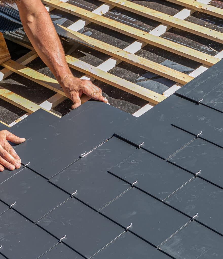 Pose de Toiture en Ardoise : Techniques et Matériaux Couvreur installant des tuiles en ardoise grise sur des liteaux de bois pour la rénovation d'une toiture.