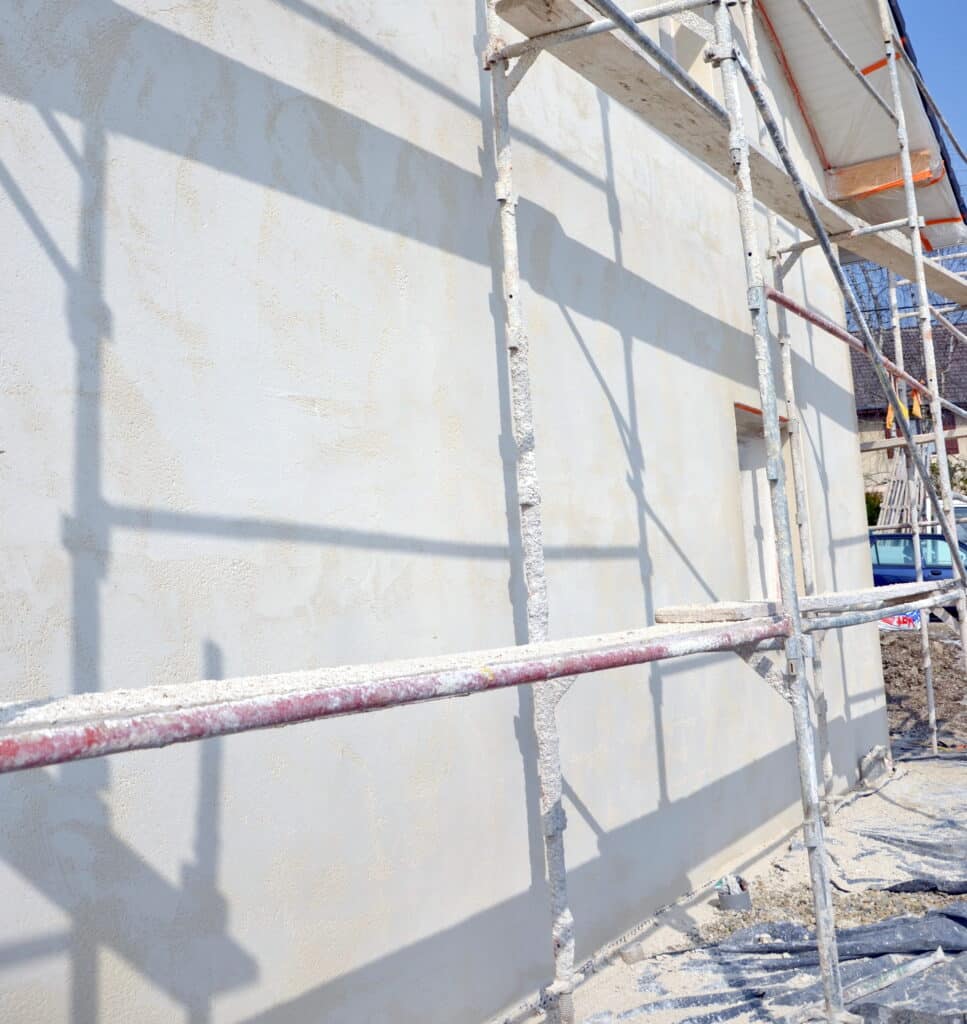 Ravalement de façade et crépi : chantier avec échafaudage Maison en cours de ravalement de façade avec échafaudage et crépi blanc neuf sous un soleil éclatant.